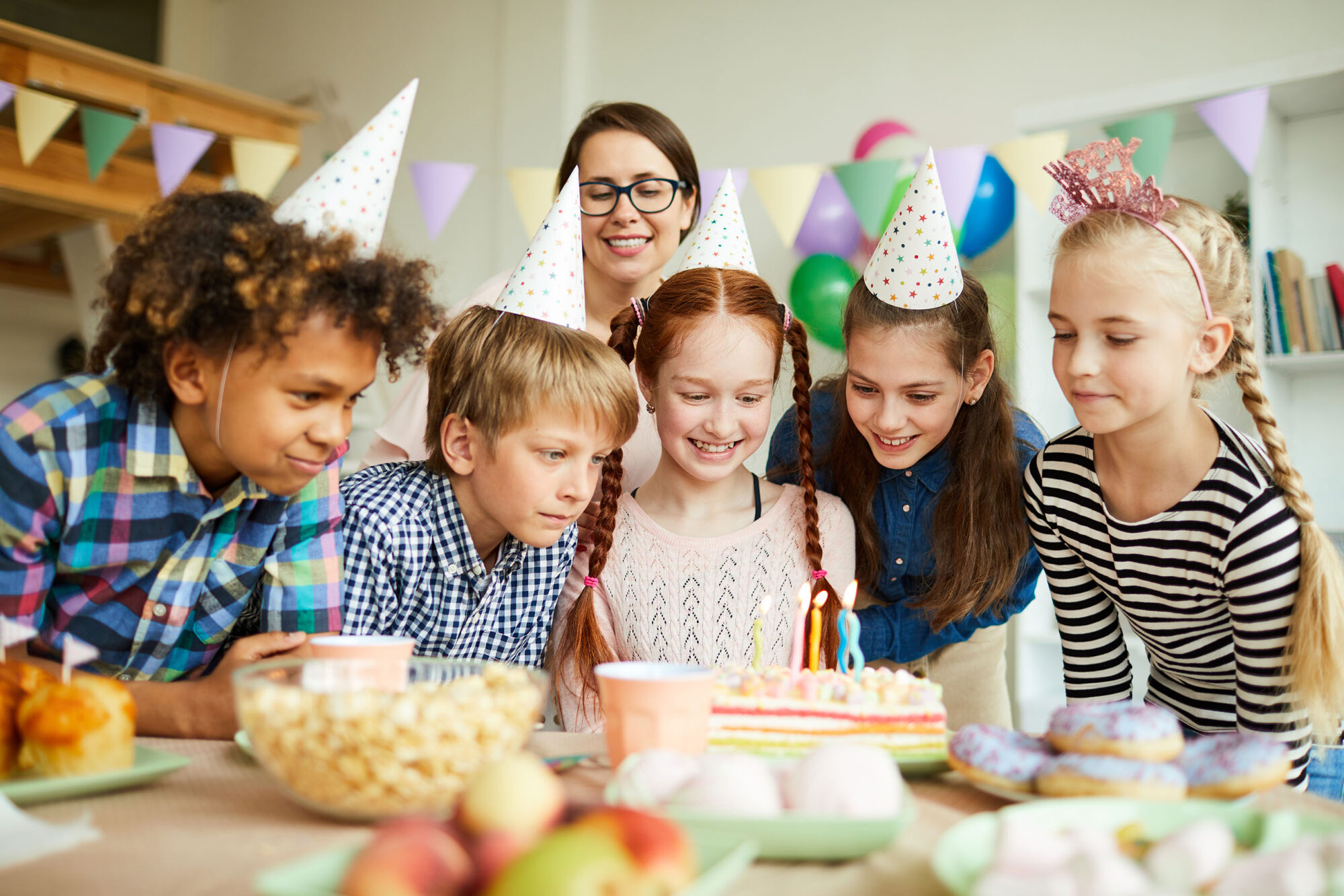 Children celebrating a birthday with a colorful cake, wearing party hats, and surrounded by snacks and decorations, highlighting the joy of cake artistry in memorable events.